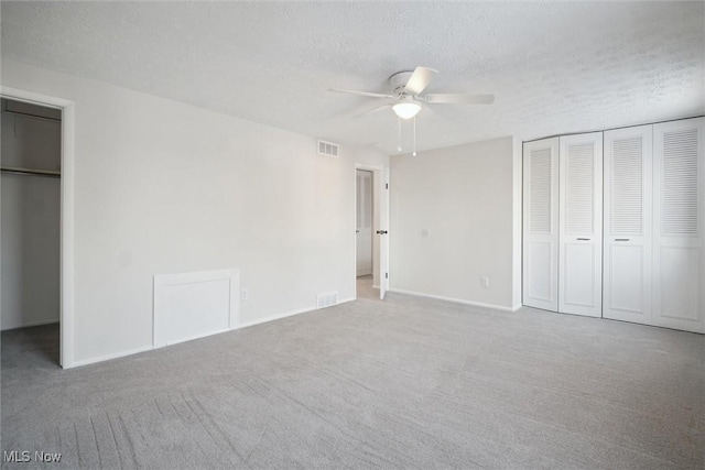 unfurnished bedroom with ceiling fan, two closets, a textured ceiling, and light carpet