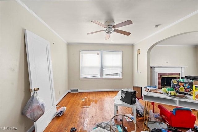 interior space featuring a brick fireplace, crown molding, ceiling fan, and light wood-type flooring