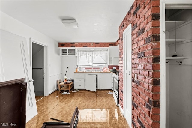 kitchen featuring white cabinets, brick wall, and range