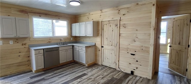 kitchen with stainless steel dishwasher, white cabinets, wooden walls, and sink