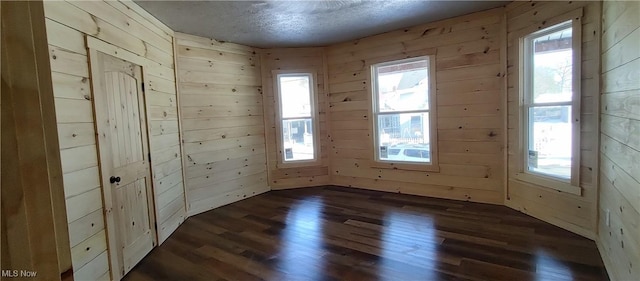 spare room featuring a textured ceiling, dark hardwood / wood-style floors, and wood walls