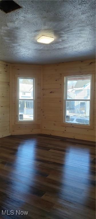 unfurnished room with wood walls and dark hardwood / wood-style floors