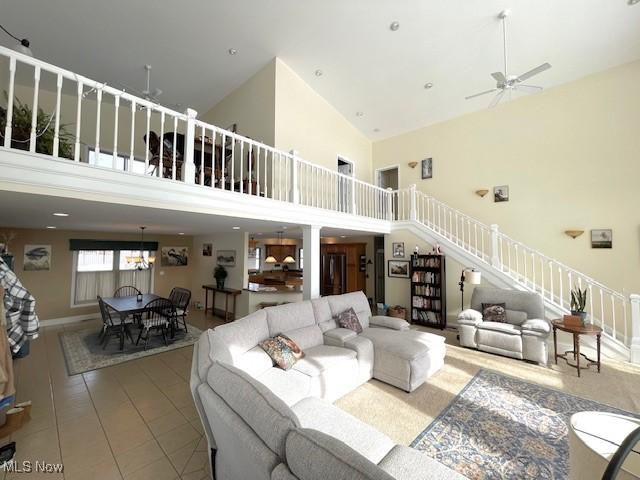 tiled living room with a towering ceiling and ceiling fan with notable chandelier