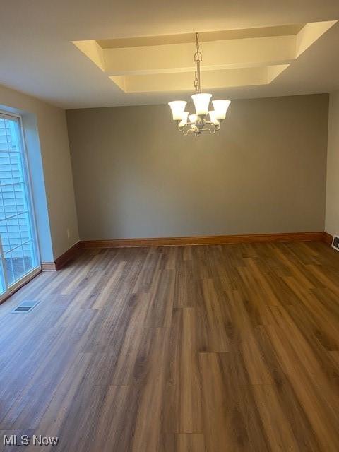 unfurnished room with a tray ceiling, plenty of natural light, dark hardwood / wood-style floors, and a chandelier