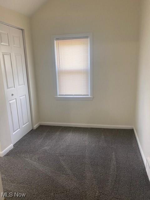 unfurnished bedroom featuring dark carpet, a closet, and vaulted ceiling