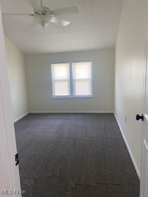 unfurnished room with ceiling fan and dark carpet