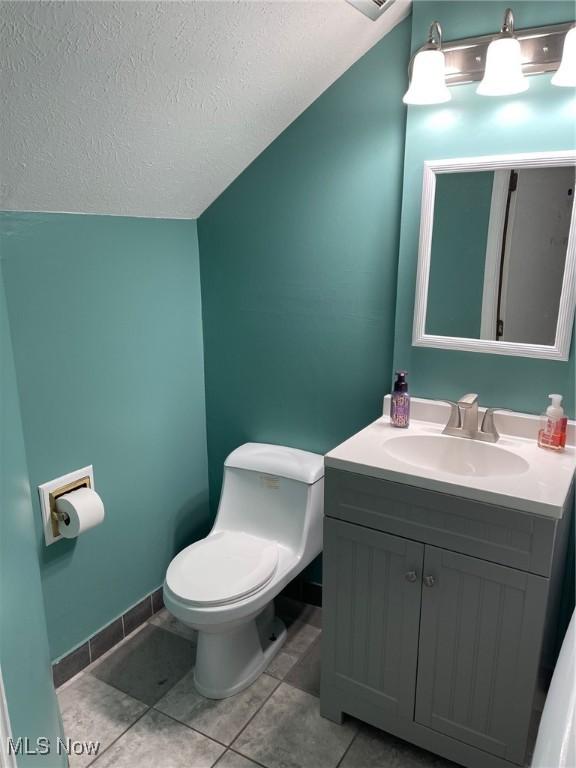 bathroom with a textured ceiling, lofted ceiling, tile patterned flooring, vanity, and toilet