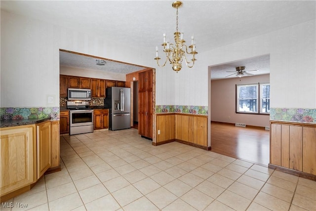 kitchen with stainless steel appliances, light tile patterned flooring, hanging light fixtures, a textured ceiling, and ceiling fan with notable chandelier