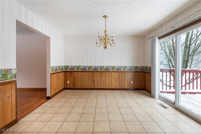 empty room featuring a textured ceiling, light tile patterned floors, and an inviting chandelier