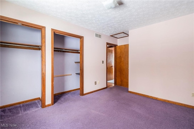 unfurnished bedroom featuring a textured ceiling, multiple closets, and carpet floors