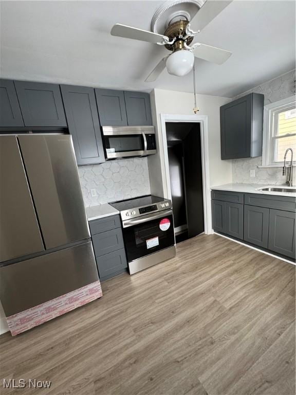 kitchen featuring ceiling fan, stainless steel appliances, tasteful backsplash, light hardwood / wood-style flooring, and sink