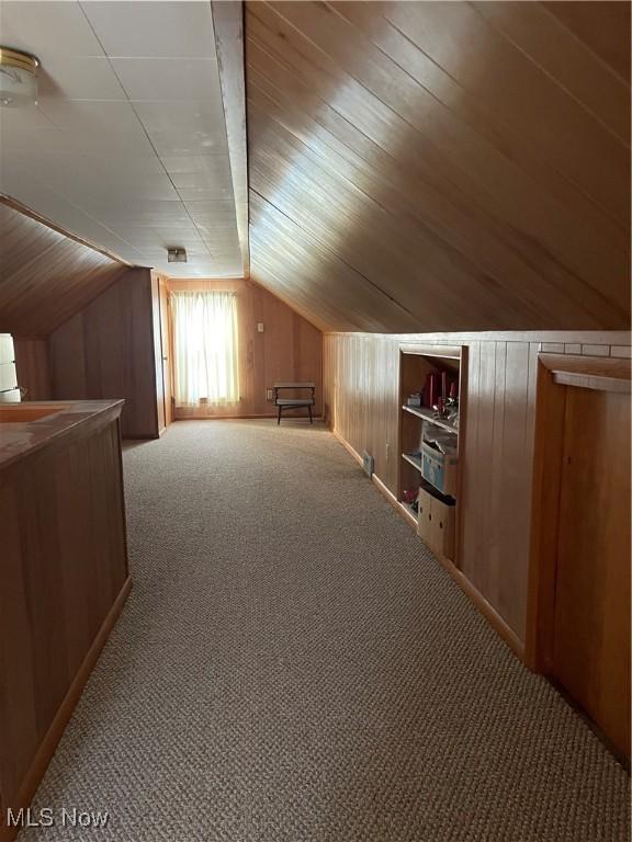 additional living space with carpet, wood walls, and vaulted ceiling