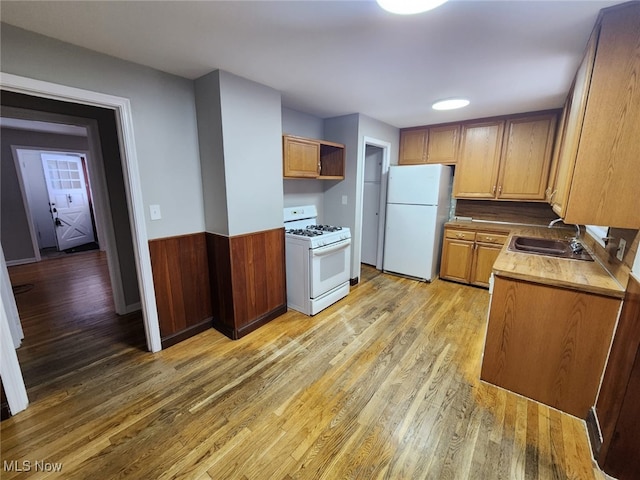 kitchen featuring wooden walls, sink, white appliances, and light hardwood / wood-style flooring