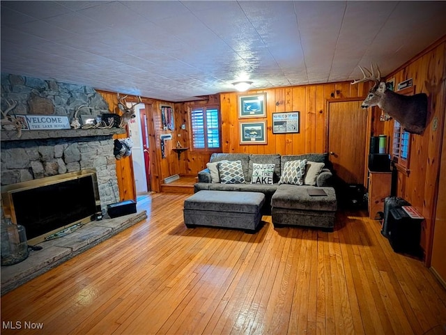 living room featuring wooden walls, a stone fireplace, and light hardwood / wood-style floors