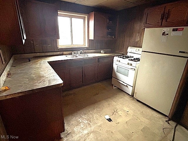 kitchen featuring sink, wood walls, dark brown cabinetry, and white appliances