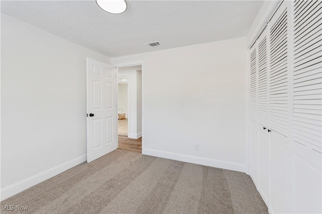 unfurnished bedroom with light colored carpet, a closet, and a textured ceiling