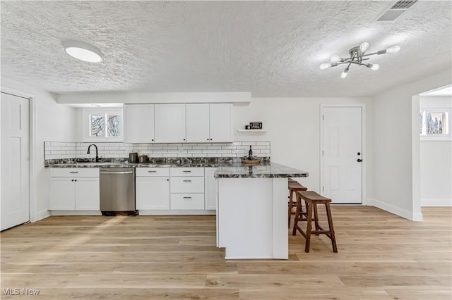 kitchen featuring a breakfast bar, dishwasher, dark stone counters, and white cabinetry