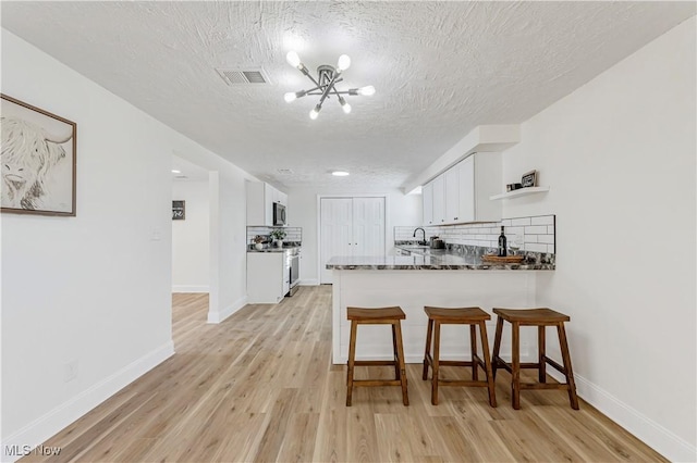 kitchen featuring white cabinetry, light hardwood / wood-style floors, kitchen peninsula, dark stone countertops, and a textured ceiling