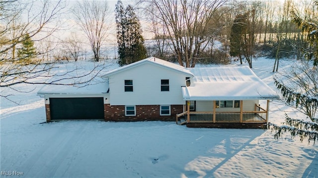 snow covered rear of property featuring a garage and a porch