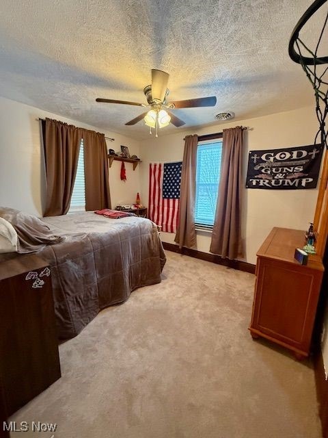 bedroom featuring light carpet, ceiling fan, a textured ceiling, and multiple windows