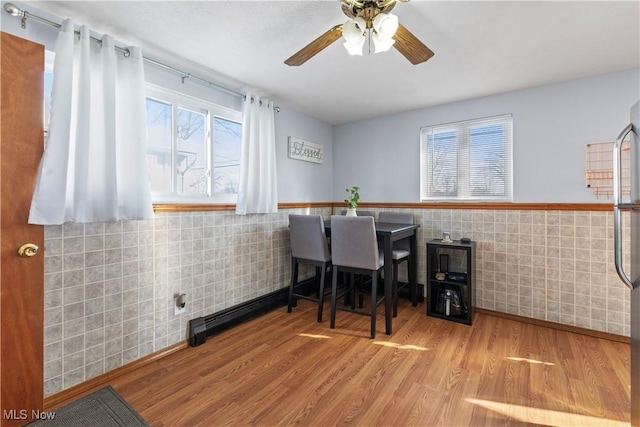 dining space featuring light wood-type flooring, tile walls, and ceiling fan