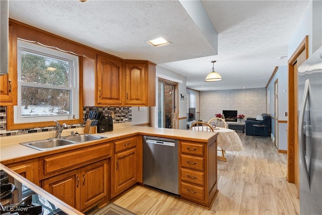 kitchen with decorative light fixtures, a fireplace, sink, light wood-type flooring, and appliances with stainless steel finishes