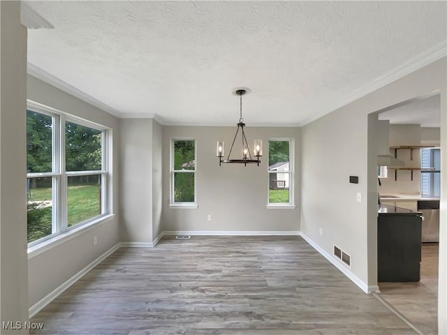 unfurnished dining area with light wood-type flooring, ornamental molding, a notable chandelier, and a healthy amount of sunlight