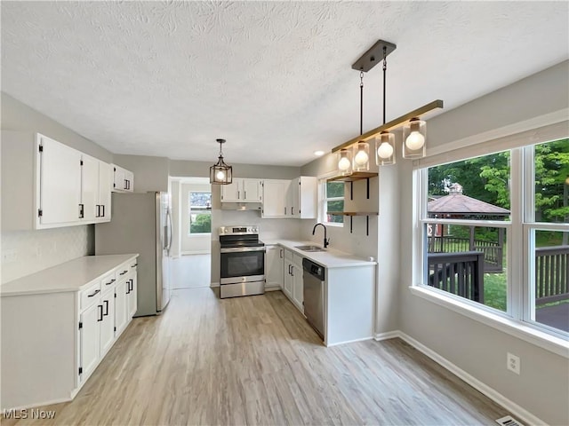 kitchen with pendant lighting, sink, white cabinetry, light wood-type flooring, and stainless steel appliances