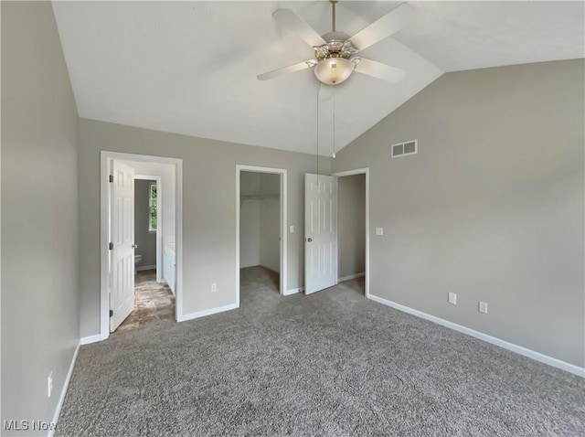 unfurnished bedroom with carpet, a walk in closet, a closet, vaulted ceiling, and ceiling fan