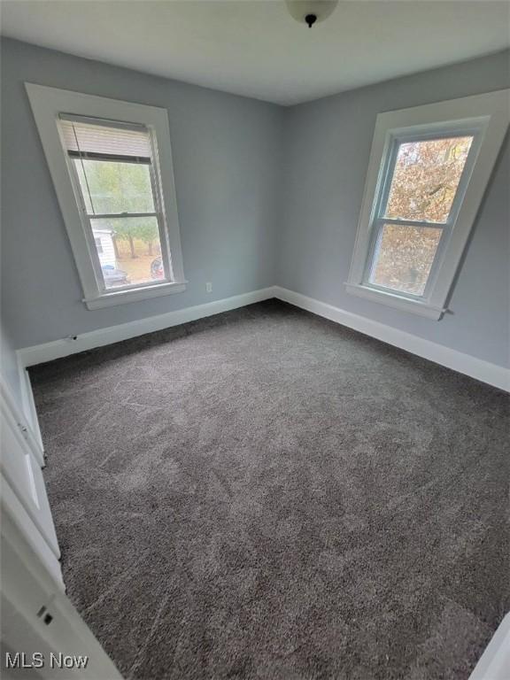 spare room with dark carpet and plenty of natural light