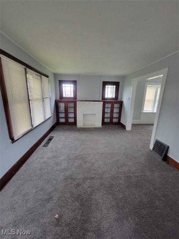 unfurnished living room featuring a brick fireplace, a wealth of natural light, and carpet floors