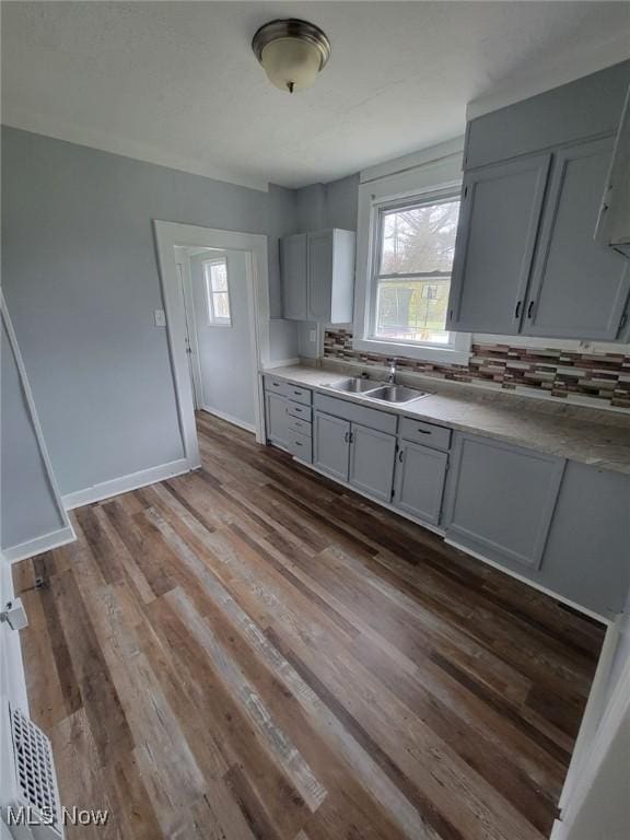 kitchen featuring dark wood-type flooring, decorative backsplash, gray cabinetry, and sink