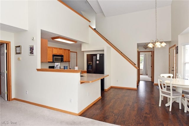 kitchen with kitchen peninsula, black refrigerator with ice dispenser, a towering ceiling, and a notable chandelier