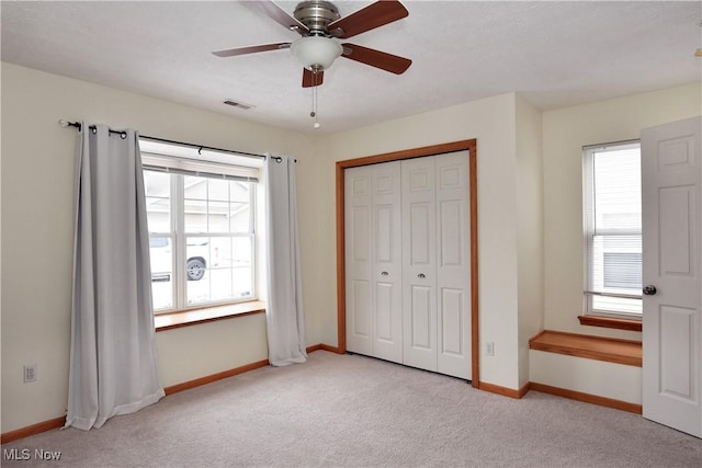 unfurnished bedroom featuring ceiling fan, multiple windows, a closet, and light carpet