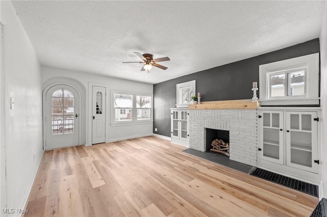 unfurnished living room with a fireplace, ceiling fan, plenty of natural light, and light wood-type flooring