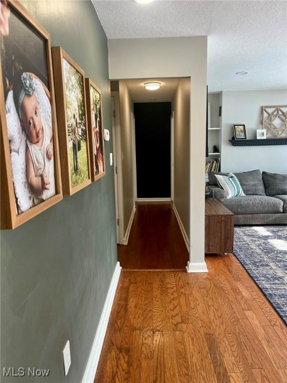 hall featuring wood-type flooring, built in features, and a textured ceiling