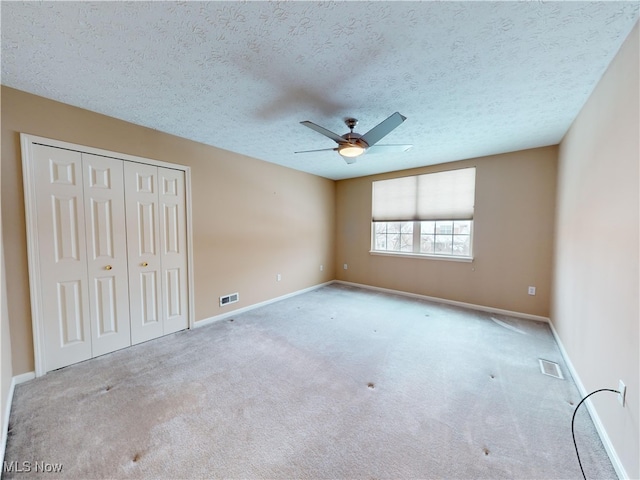 unfurnished bedroom featuring ceiling fan, light carpet, a closet, and a textured ceiling