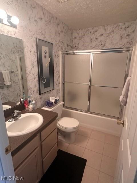 full bathroom featuring toilet, combined bath / shower with glass door, tile patterned floors, a textured ceiling, and vanity