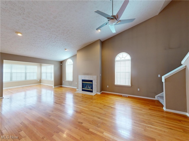 unfurnished living room featuring ceiling fan, a fireplace, light hardwood / wood-style floors, a textured ceiling, and high vaulted ceiling