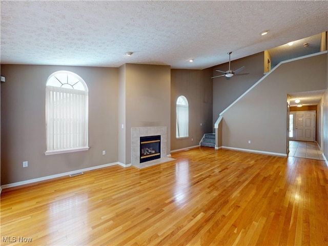 unfurnished living room with a textured ceiling, lofted ceiling, light hardwood / wood-style floors, and a tile fireplace