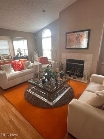 living room featuring a textured ceiling, lofted ceiling, a fireplace, and wood-type flooring