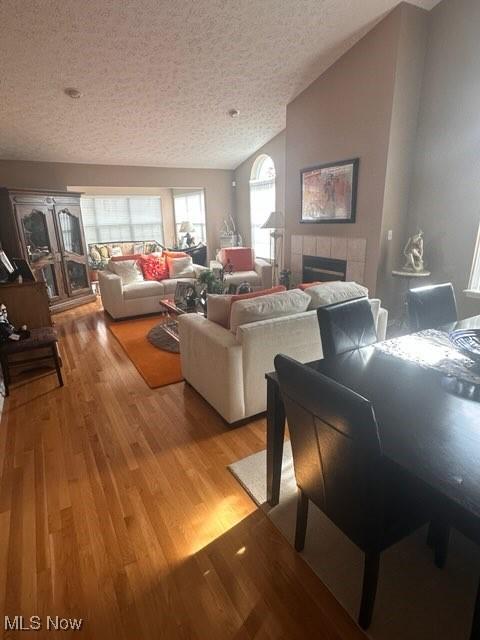 living room with lofted ceiling, a tile fireplace, a textured ceiling, and light hardwood / wood-style floors