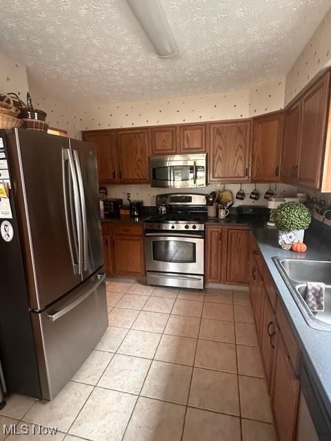 kitchen with light tile patterned floors, sink, a textured ceiling, and appliances with stainless steel finishes