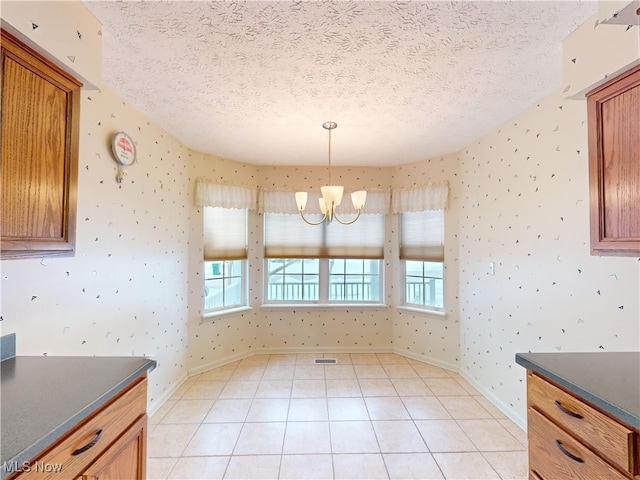 unfurnished dining area featuring a textured ceiling, light tile patterned floors, and a chandelier