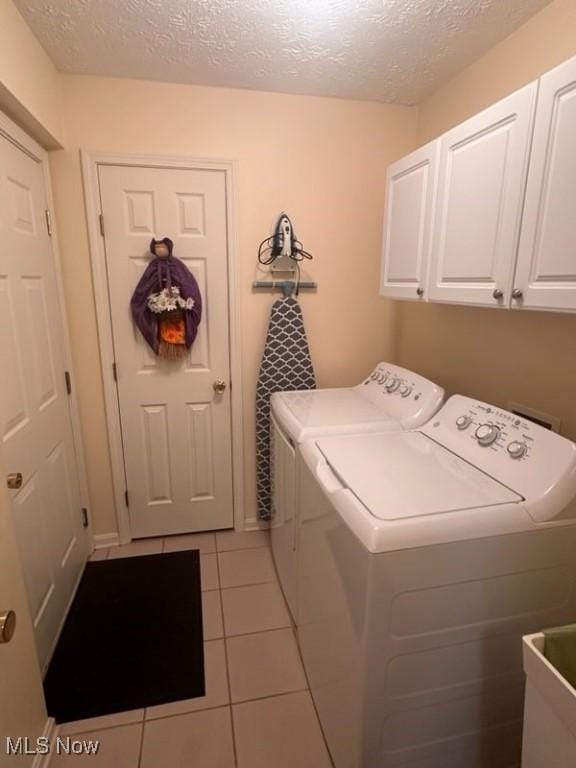 laundry area featuring light tile patterned floors, cabinets, a textured ceiling, and washer and clothes dryer