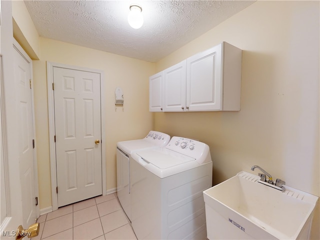 washroom featuring sink, washing machine and clothes dryer, a textured ceiling, light tile patterned floors, and cabinets