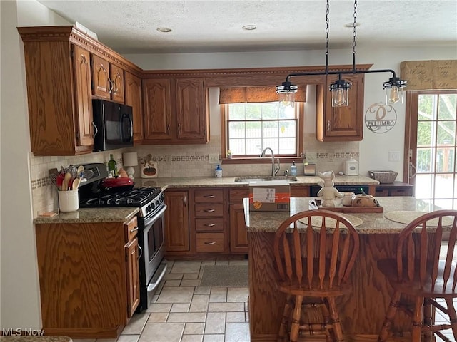 kitchen with stainless steel range with gas cooktop, a breakfast bar area, a center island, hanging light fixtures, and sink