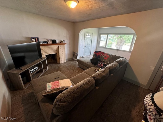 living room with a brick fireplace, a textured ceiling, and dark hardwood / wood-style flooring