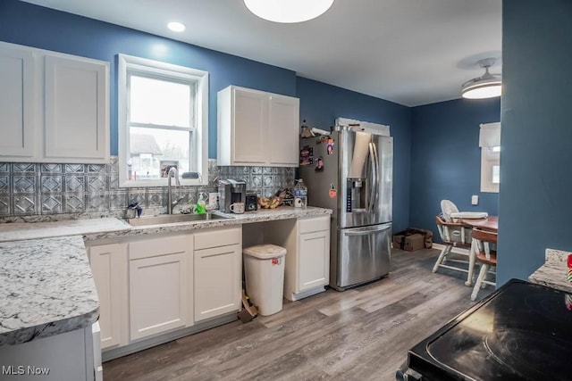 kitchen featuring backsplash, stainless steel refrigerator with ice dispenser, sink, black electric range oven, and white cabinetry