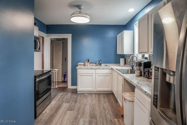 kitchen with light hardwood / wood-style floors, sink, white cabinetry, appliances with stainless steel finishes, and light stone counters